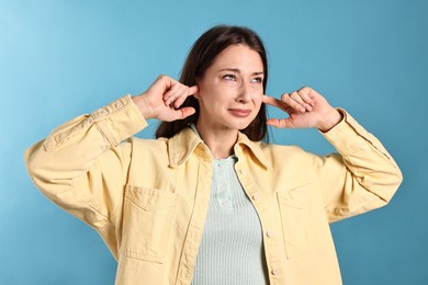 Photo of Annoyed woman covering her ears due to loud sound on light blue background