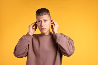 Photo of Annoyed young man covering his ears due to loud sound on orange background