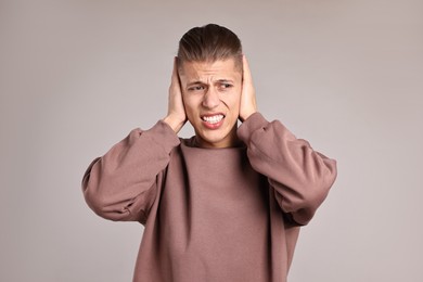 Photo of Annoyed young man covering his ears due to loud sound on light grey background