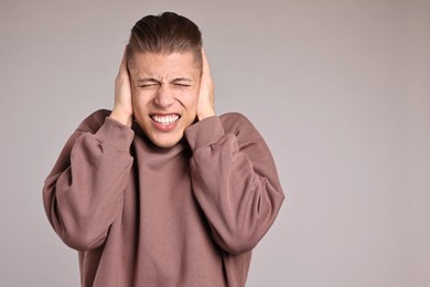 Photo of Annoyed young man covering his ears due to loud sound on light grey background