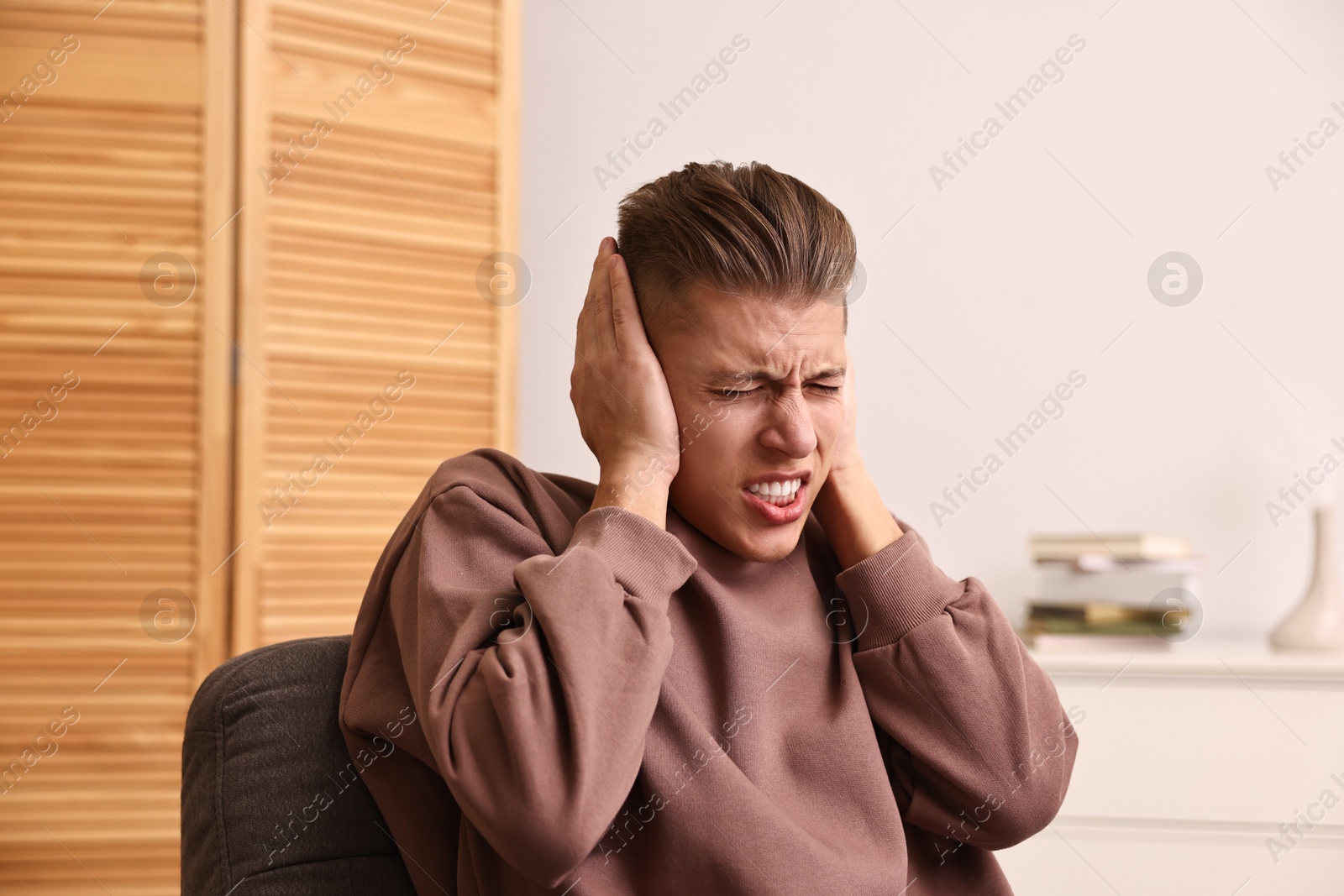 Photo of Annoyed young man covering his ears due to loud sound at home