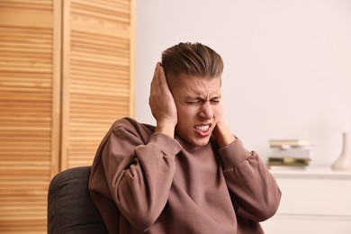 Photo of Annoyed young man covering his ears due to loud sound at home