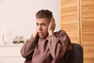 Photo of Annoyed young man covering his ears due to loud sound at home