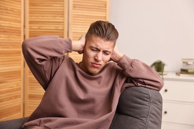 Photo of Annoyed young man covering his ears due to loud sound at home