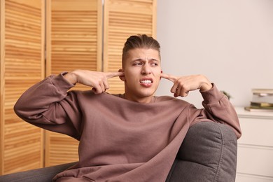 Photo of Annoyed young man covering his ears due to loud sound at home