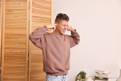 Photo of Annoyed young man covering his ears due to loud sound at home