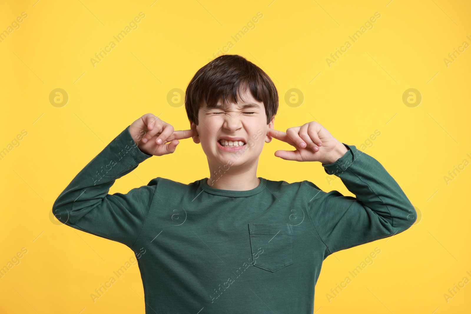 Photo of Annoyed boy covering his ears due to loud sound on yellow background