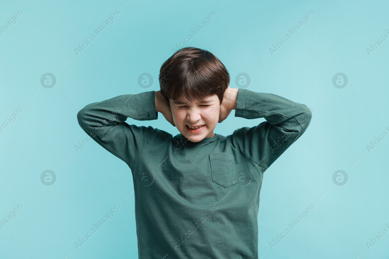 Photo of Annoyed boy covering his ears due to loud sound on light blue background