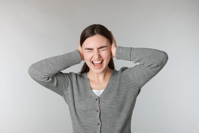 Photo of Distressed woman covering her ears from loud noise on light grey background