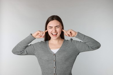 Photo of Distressed woman covering her ears from loud noise on light grey background