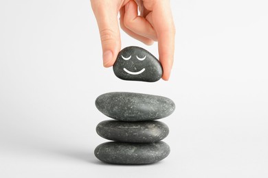 Photo of Woman putting rock with smiley face onto cairn against light background, closeup. Harmony and life balance