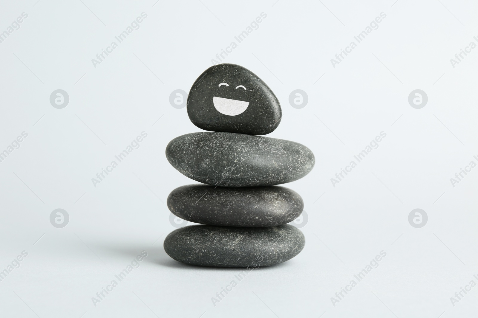 Photo of Stack of rocks with drawn smiley face on light background. Harmony and life balance