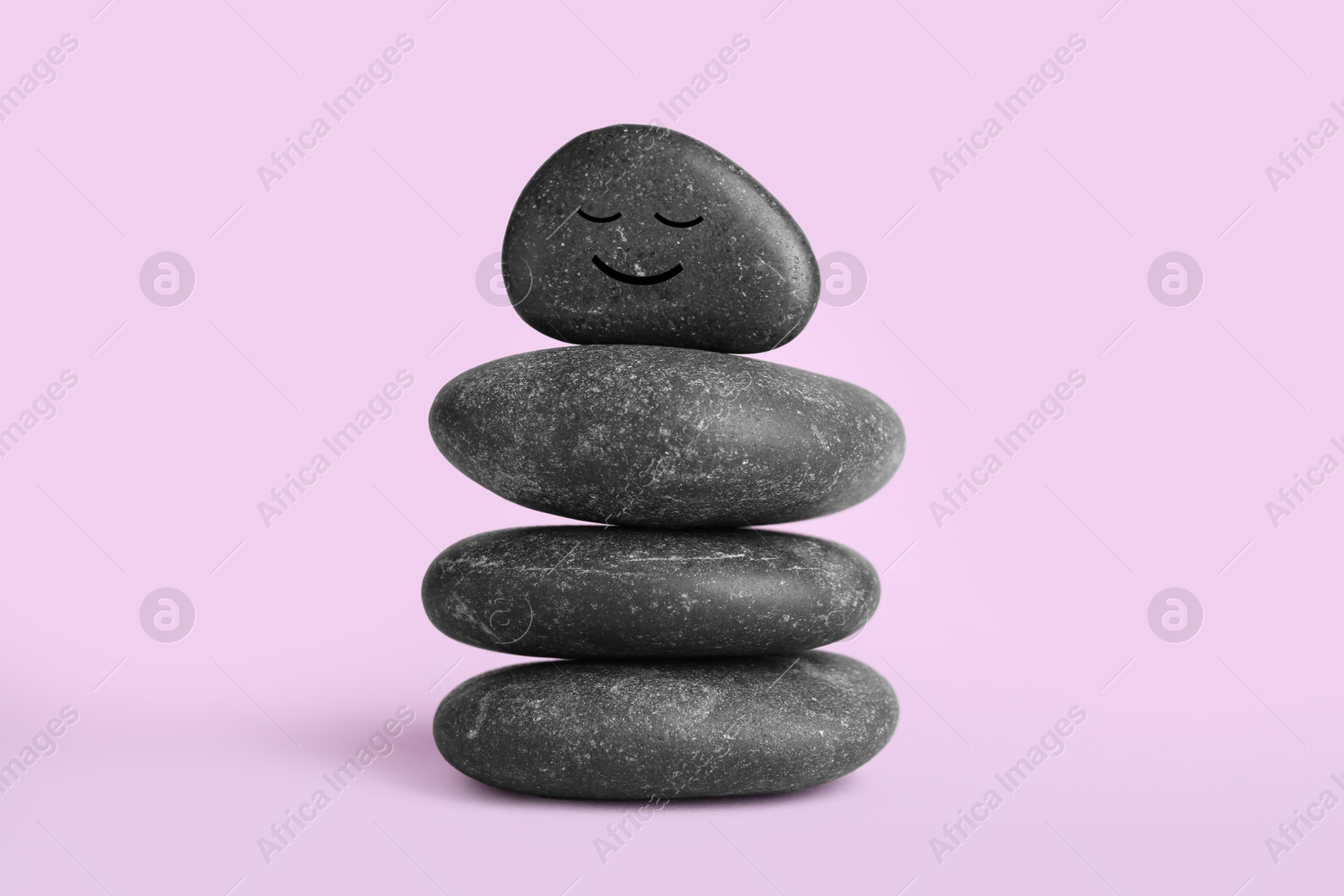 Photo of Stack of rocks with drawn smiley face on lilac background. Harmony and life balance