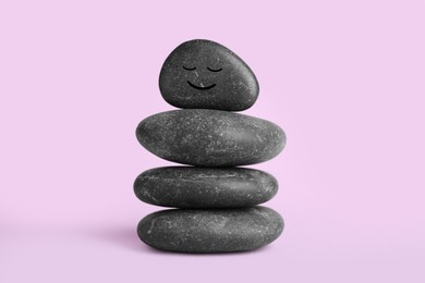 Photo of Stack of rocks with drawn smiley face on lilac background. Harmony and life balance