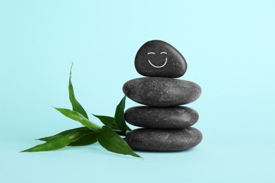 Photo of Stack of rocks with drawn smiley face on light blue background. Harmony and life balance