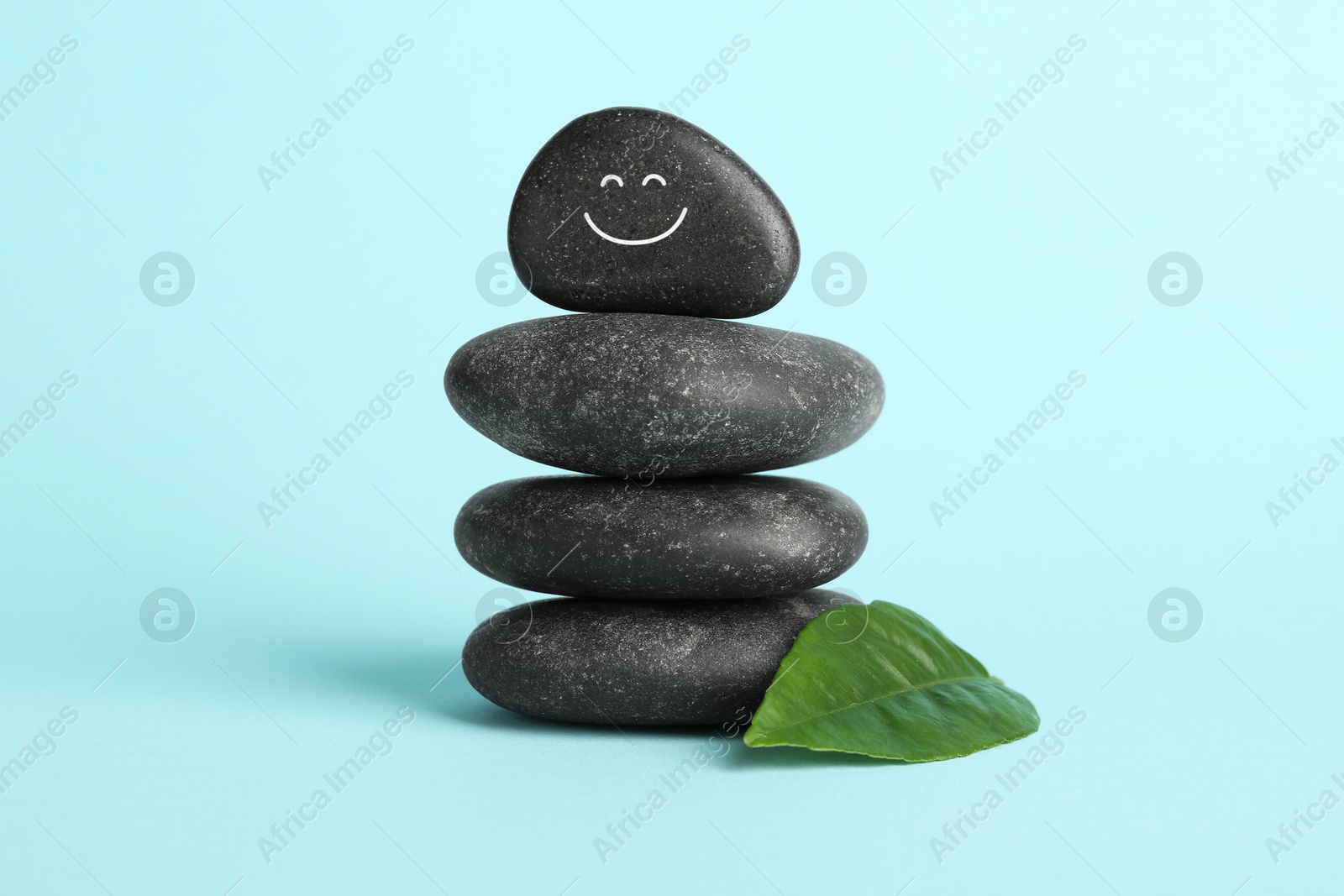 Photo of Stack of rocks with drawn smiley face on light blue background. Harmony and life balance