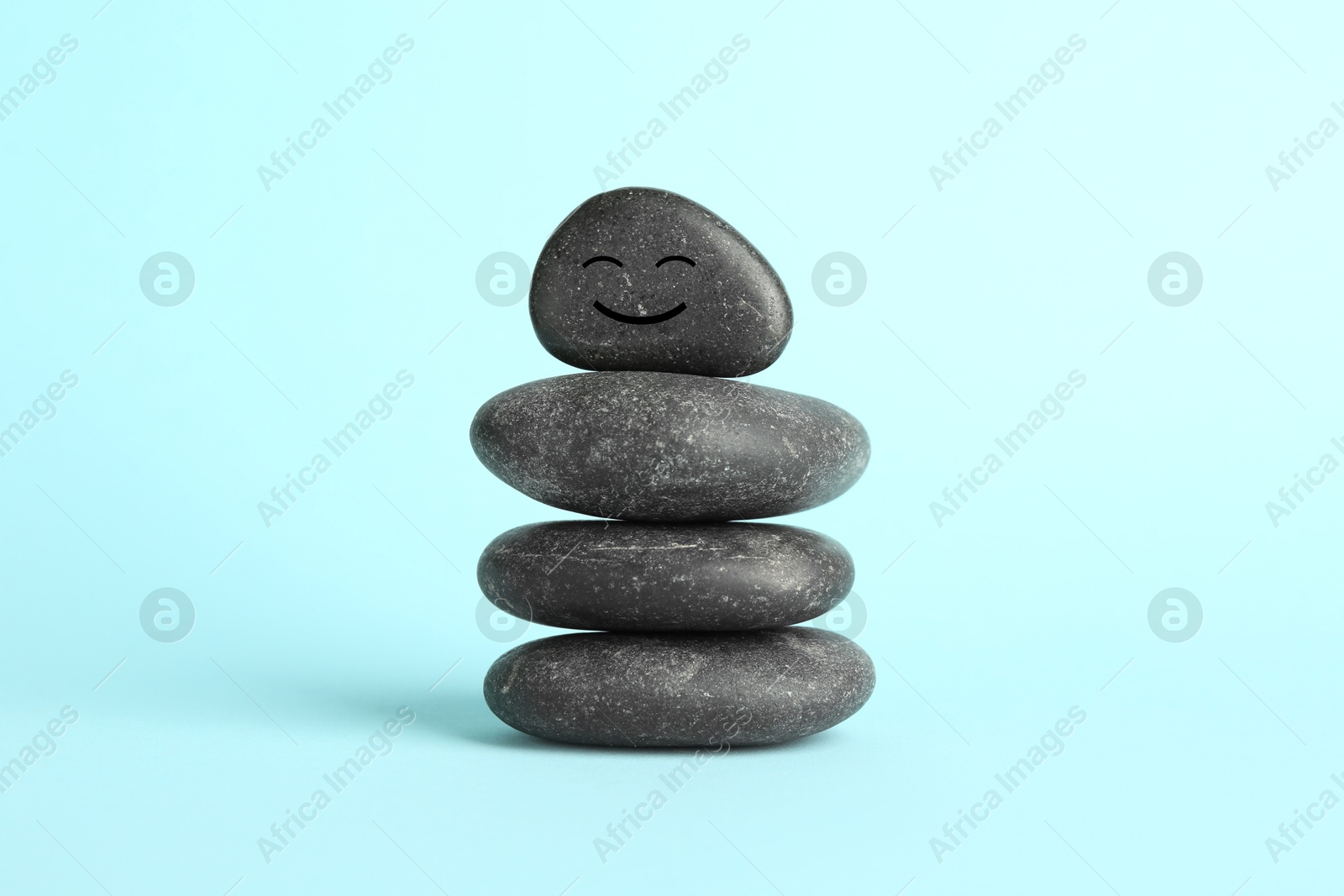 Photo of Stack of rocks with drawn smiley face on light blue background. Harmony and life balance