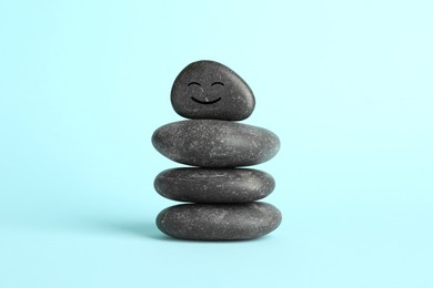 Photo of Stack of rocks with drawn smiley face on light blue background. Harmony and life balance