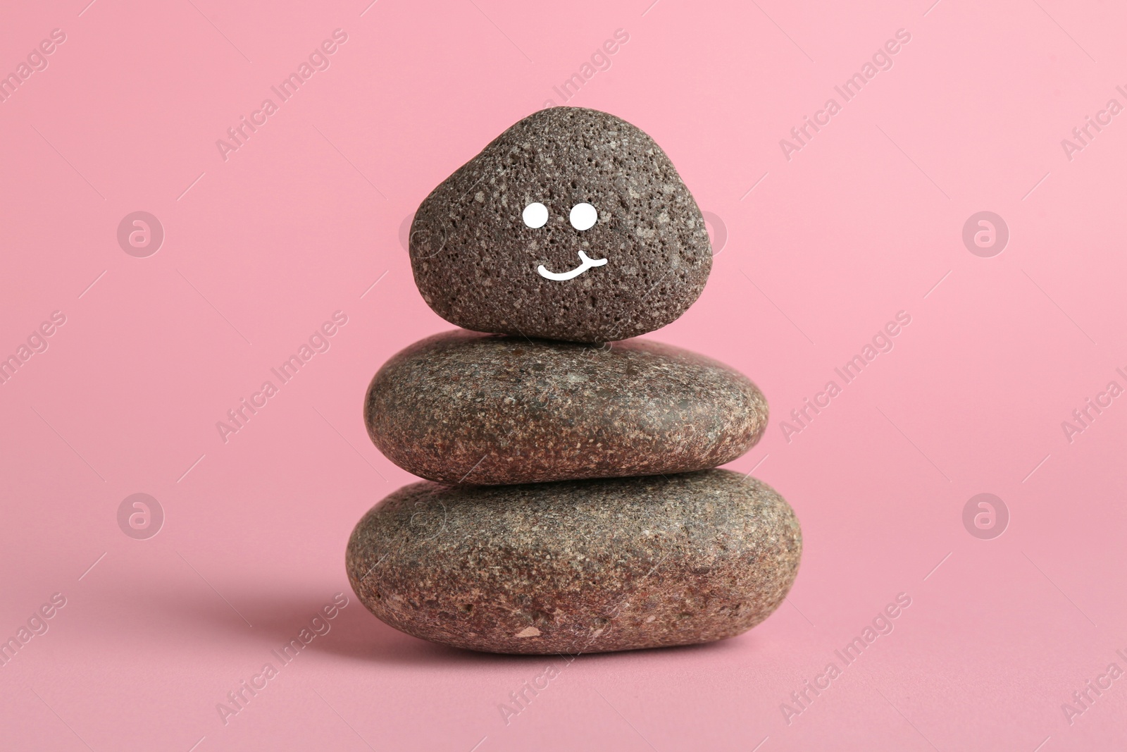 Photo of Stack of rocks with drawn smiley face on light pink background. Harmony and life balance