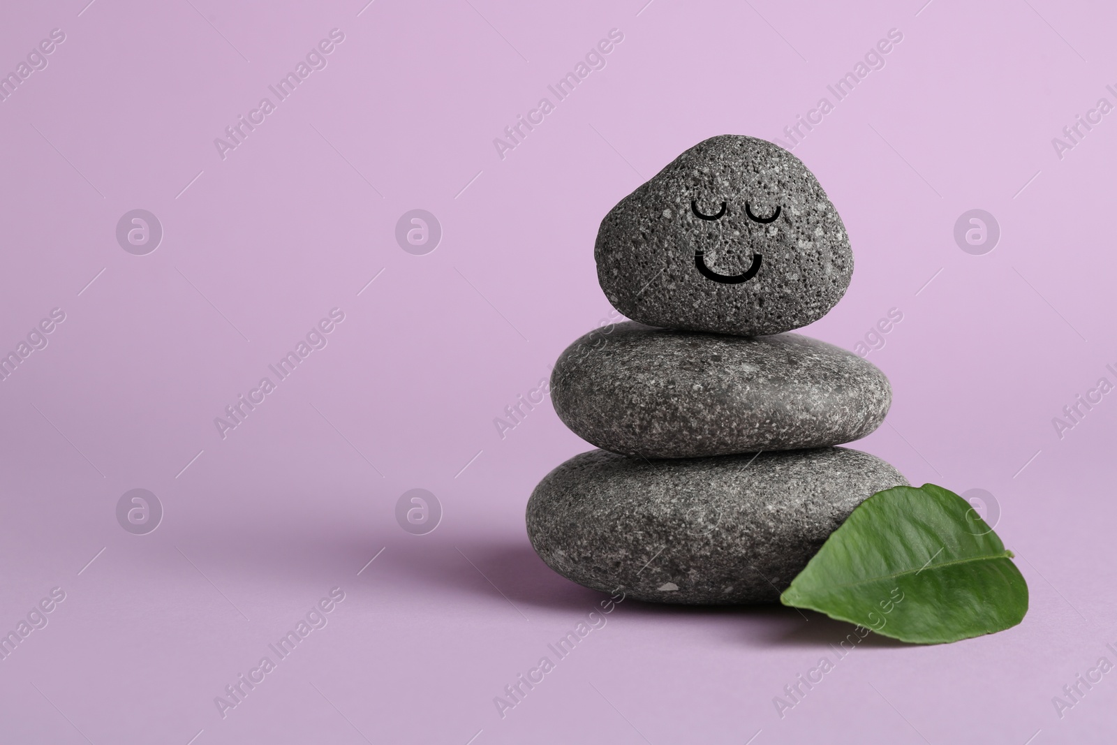 Photo of Stack of rocks with drawn smiley face on lilac background, space for text. Harmony and life balance