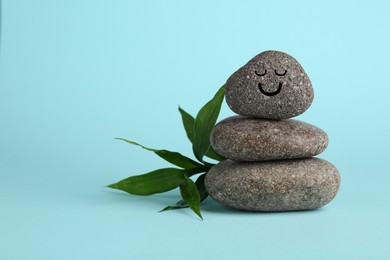 Photo of Stack of rocks with drawn smiley face on light blue background, space for text. Harmony and life balance