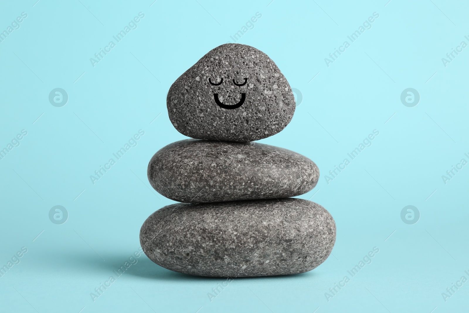 Photo of Stack of rocks with drawn smiley face on light blue background. Harmony and life balance