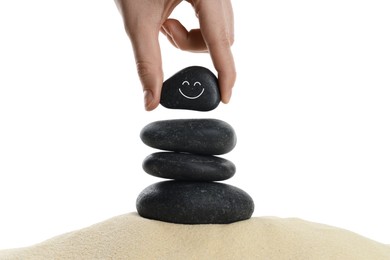 Photo of Woman putting stone with drawn smiley face on stack against white background, closeup. Harmony and life balance