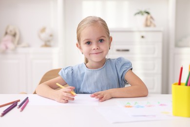 Photo of Cute girl drawing at white table in kindergarten