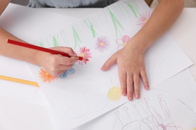 Photo of Girl drawing flowers at white table indoors, closeup