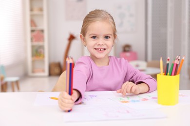 Photo of Smiling girl at white table with drawing and pencils in kindergarten