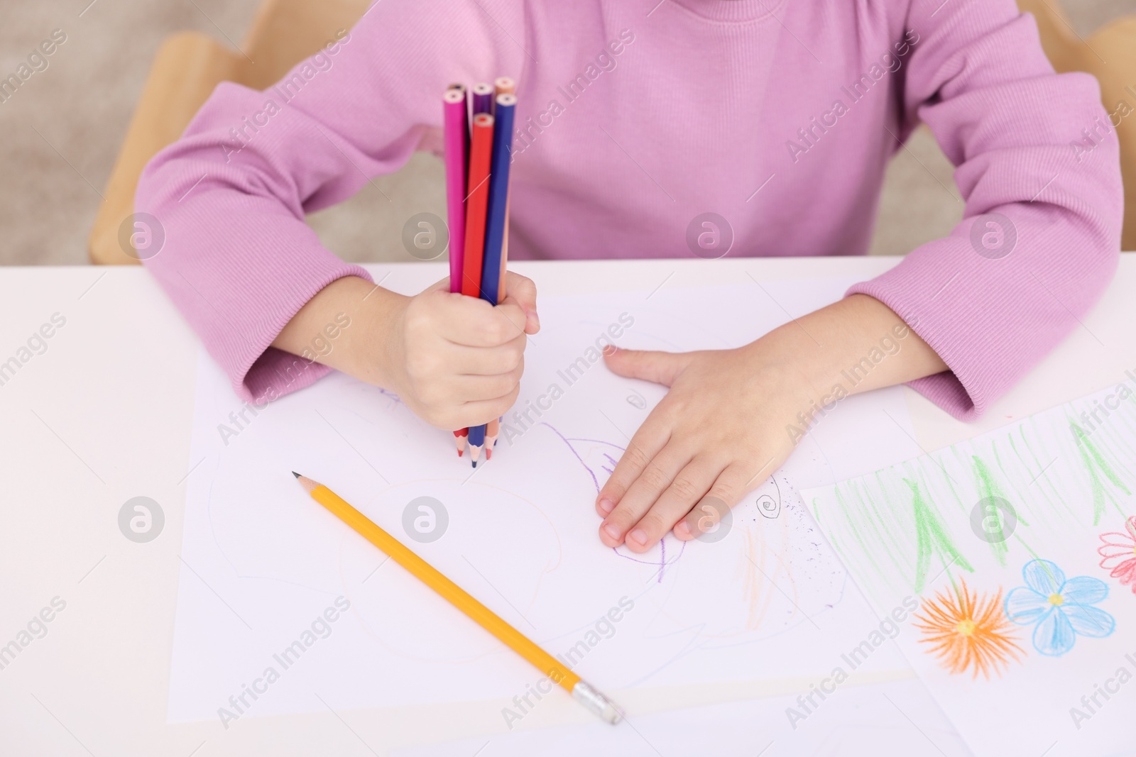 Photo of Girl drawing with pencils at white table indoors, closeup