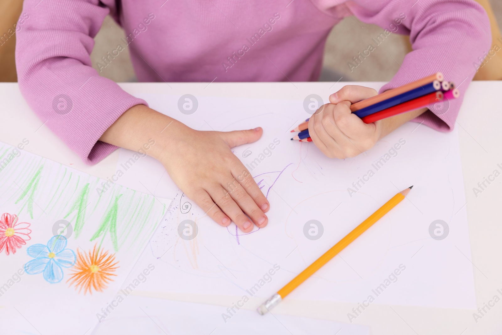 Photo of Girl drawing with pencils at white table indoors, closeup