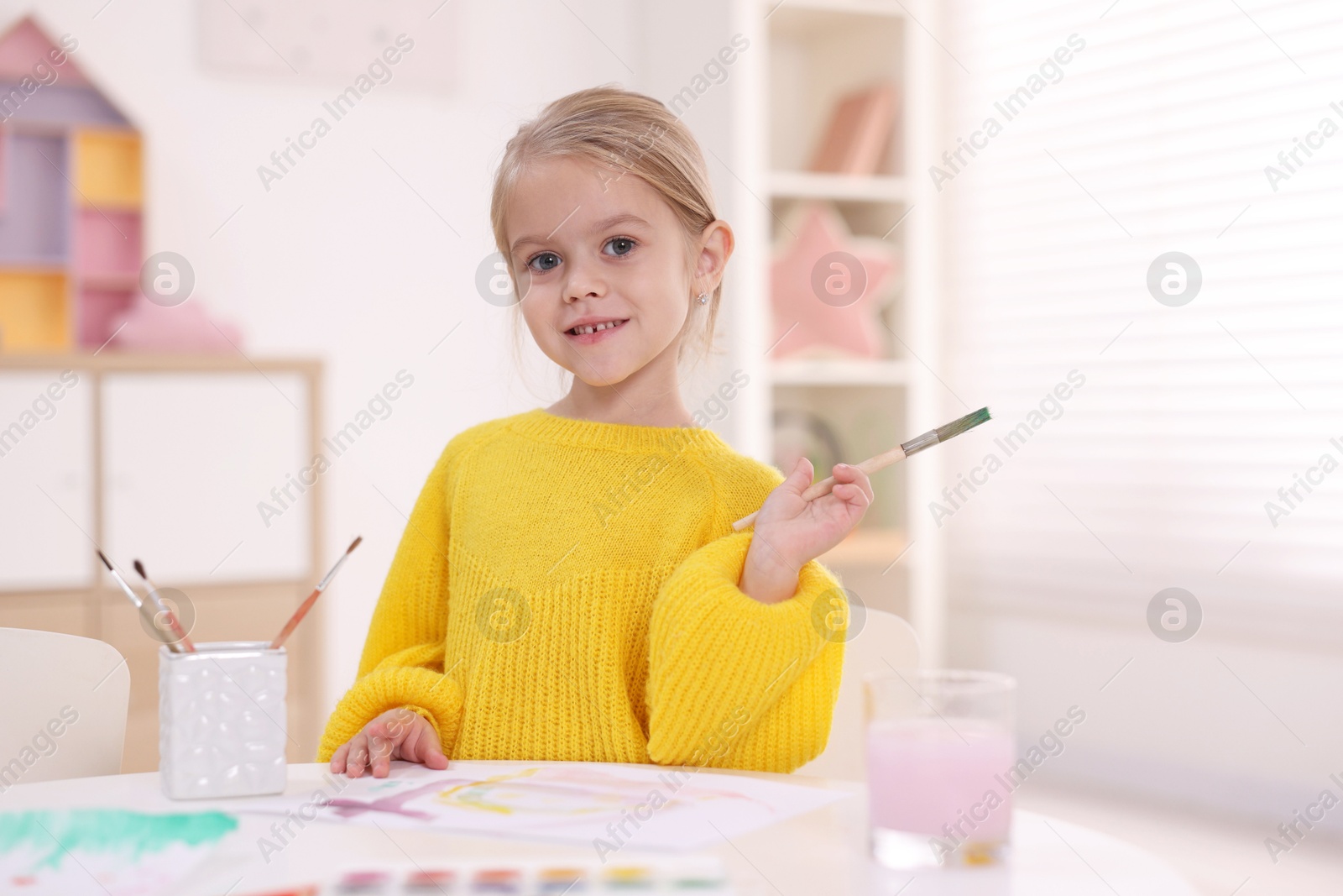 Photo of Smiling girl drawing at white table in kindergarten