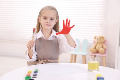 Photo of Cute girl drawing with palm at white table in kindergarten