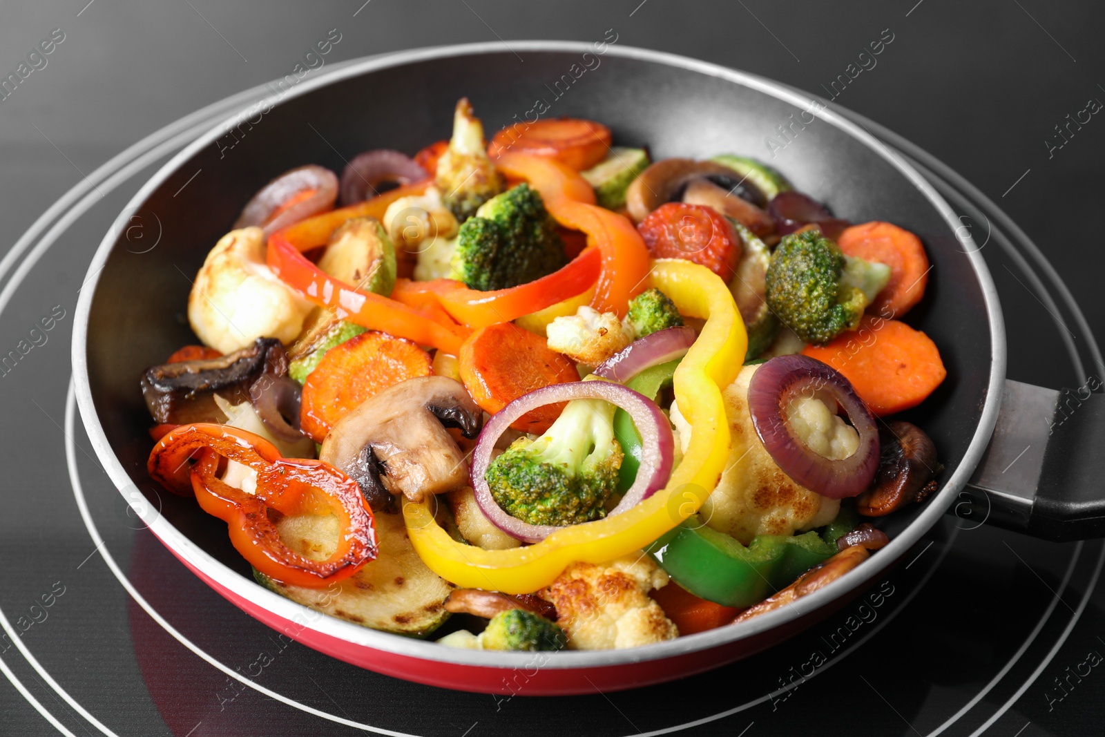 Photo of Frying pan with mix of vegetables and mushrooms on cooktop, closeup