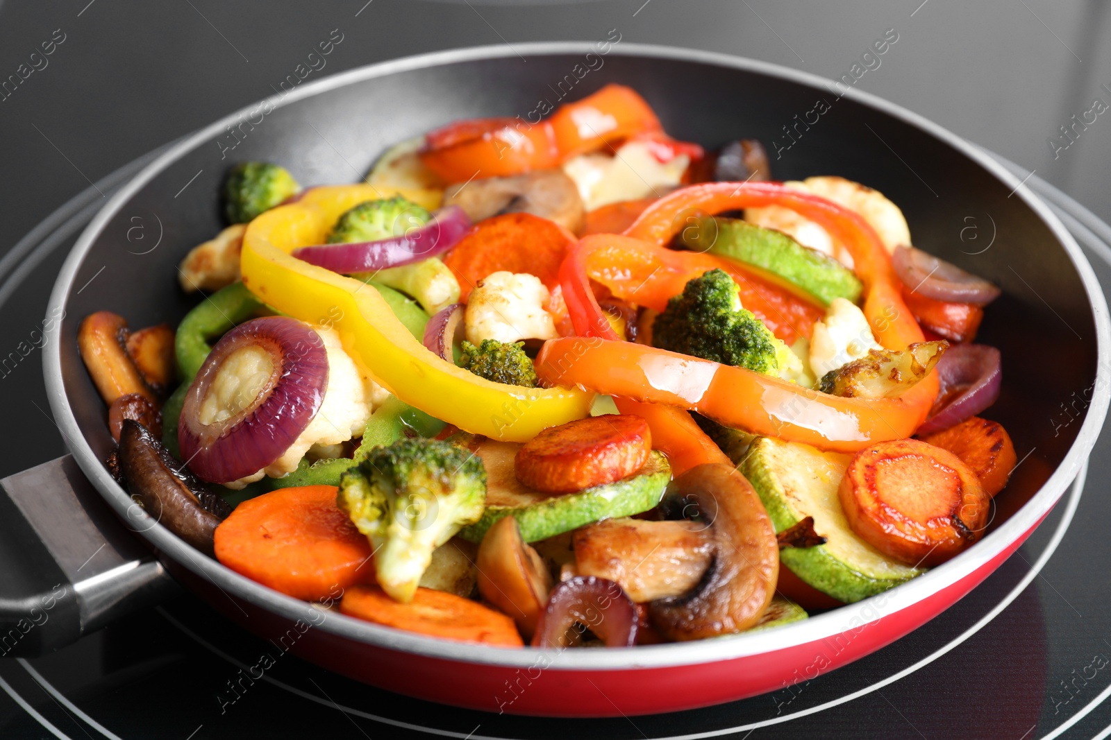 Photo of Frying pan with mix of vegetables and mushrooms on cooktop, closeup