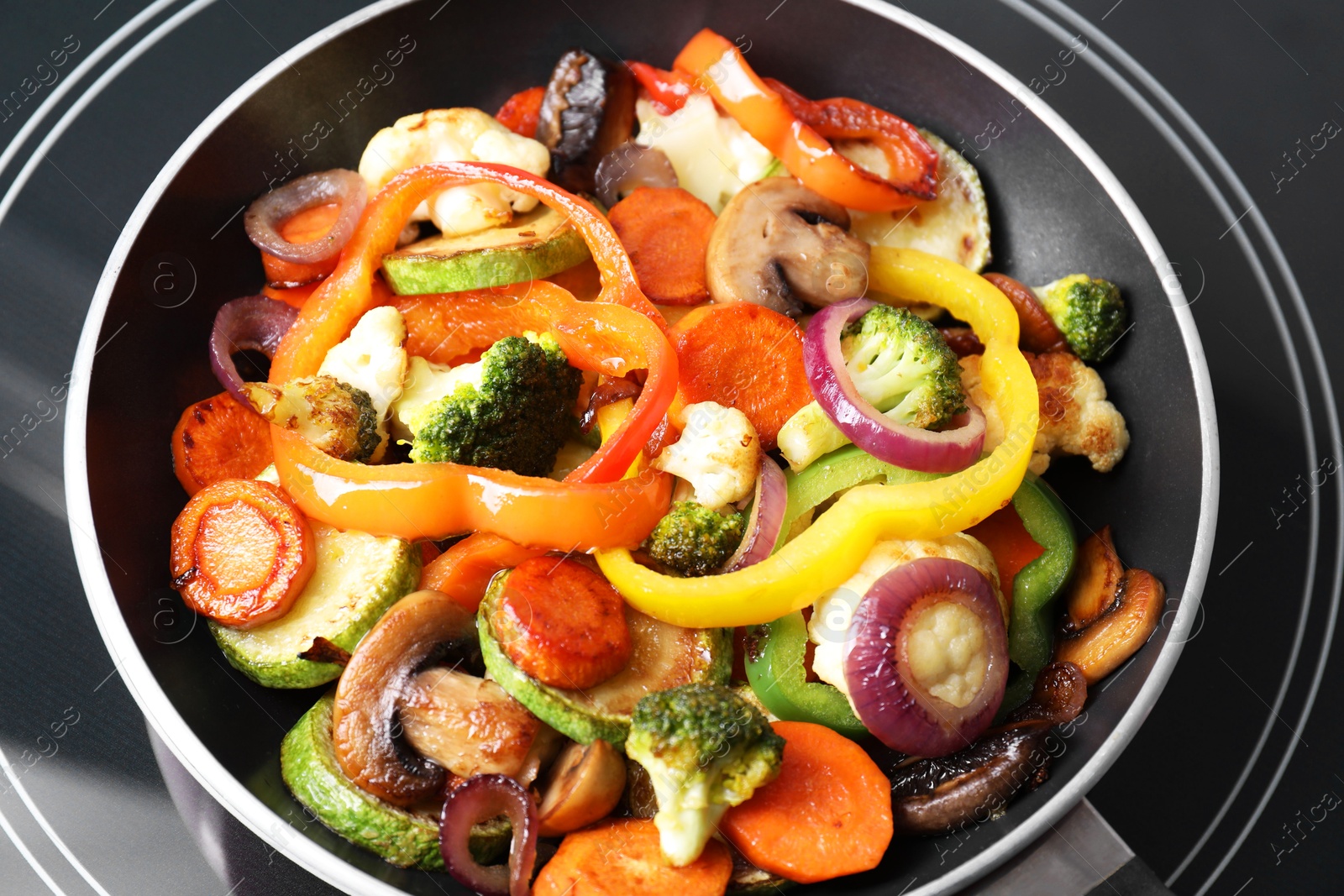 Photo of Frying pan with mix of vegetables and mushrooms on cooktop, closeup