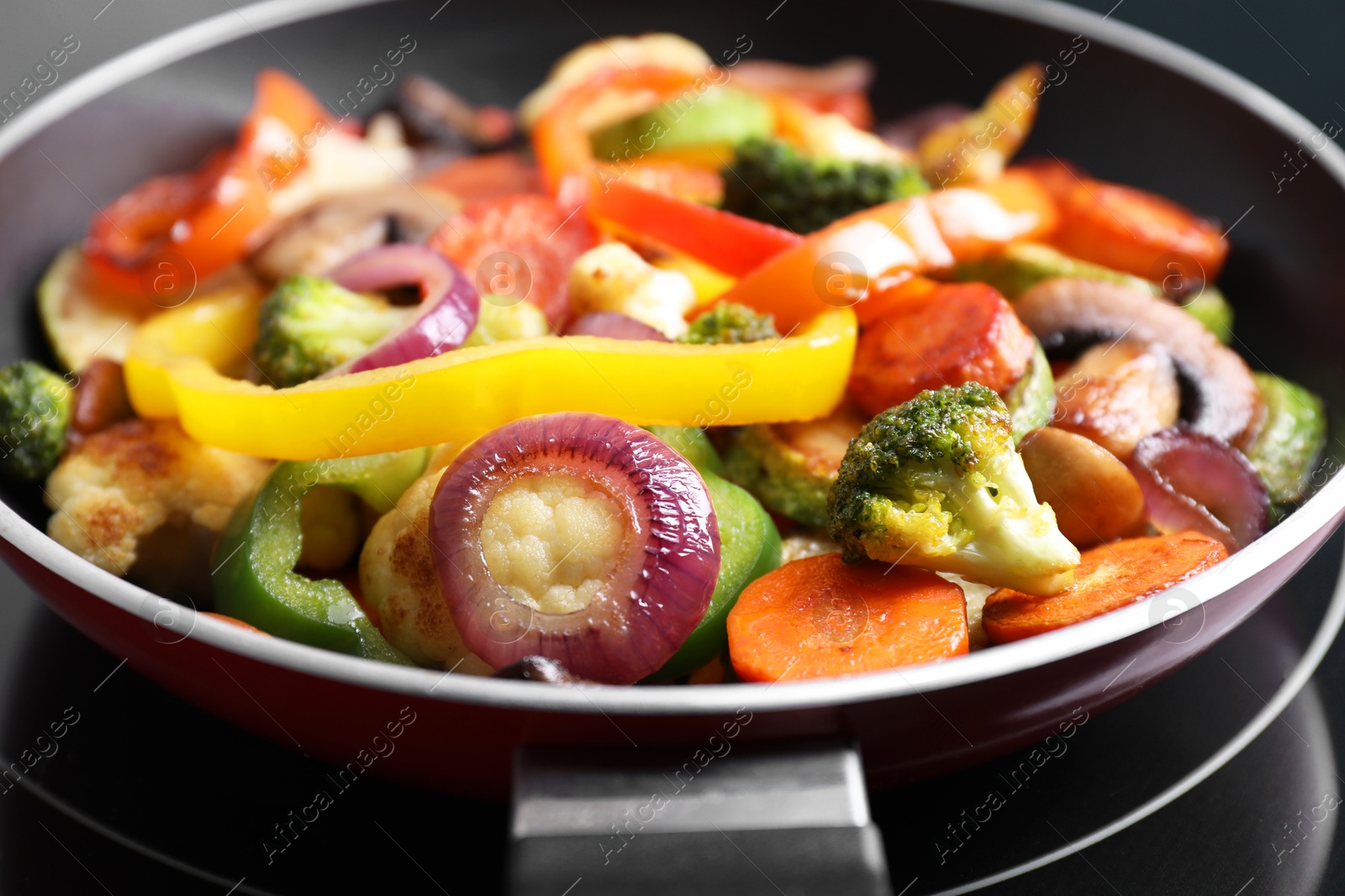 Photo of Frying pan with mix of vegetables and mushrooms on cooktop, closeup