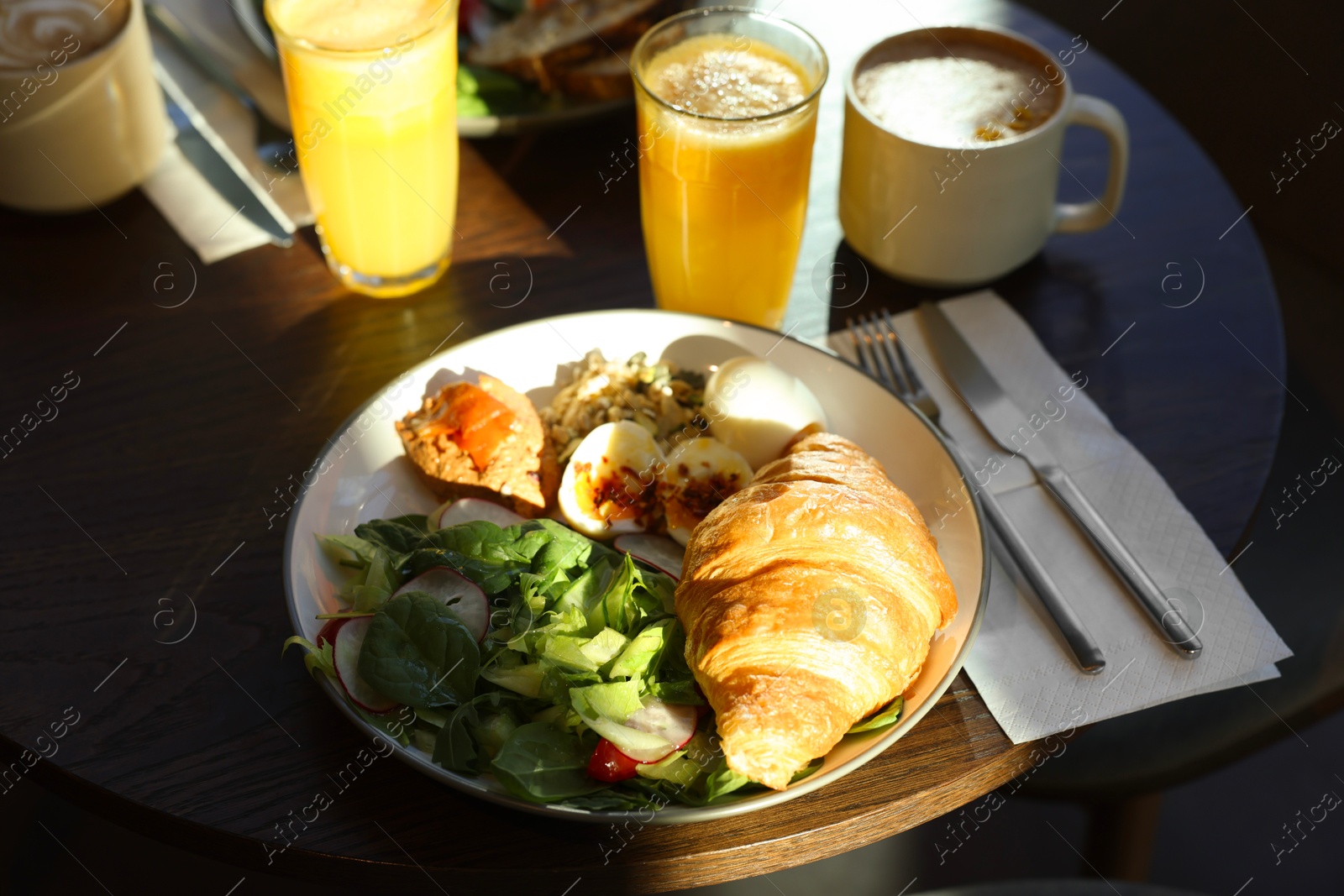 Photo of Tasty breakfast. Freshly baked croissant and salad served on wooden table in cafe, closeup