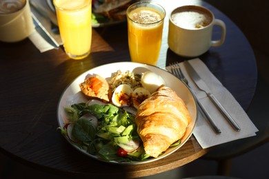 Photo of Tasty breakfast. Freshly baked croissant and salad served on wooden table in cafe, closeup