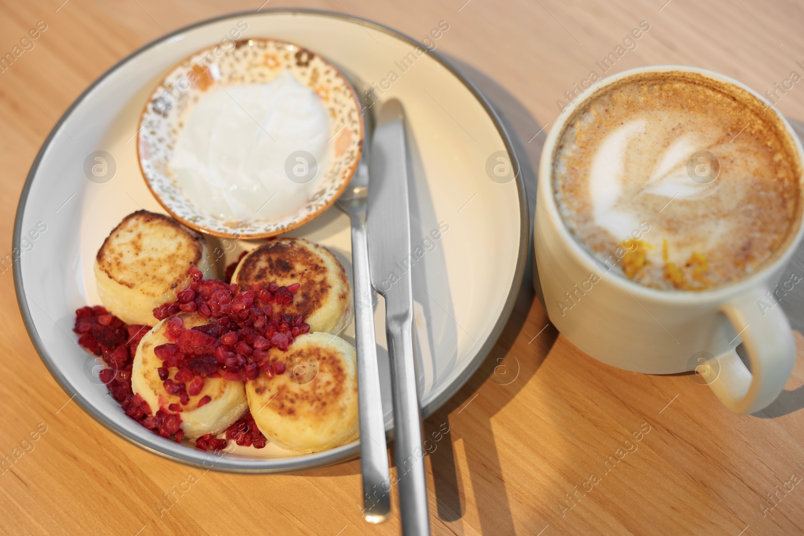 Photo of Delicious cottage cheese pancakes and tasty latte served on wooden table in cafe, closeup