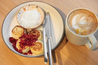 Photo of Delicious cottage cheese pancakes and tasty latte served on wooden table in cafe, closeup