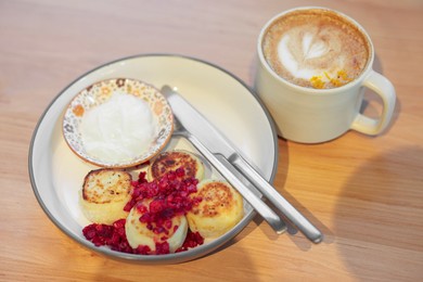 Photo of Delicious cottage cheese pancakes and tasty latte served on wooden table in cafe, closeup