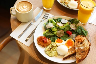 Photo of Tasty breakfast. Salad and eggs with red caviar served on wooden table in cafe, closeup