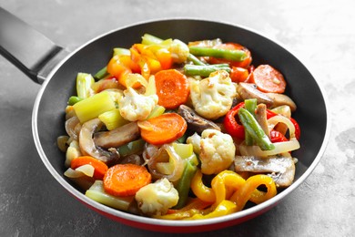 Photo of Different vegetables and mushrooms in frying pan on grey table, closeup