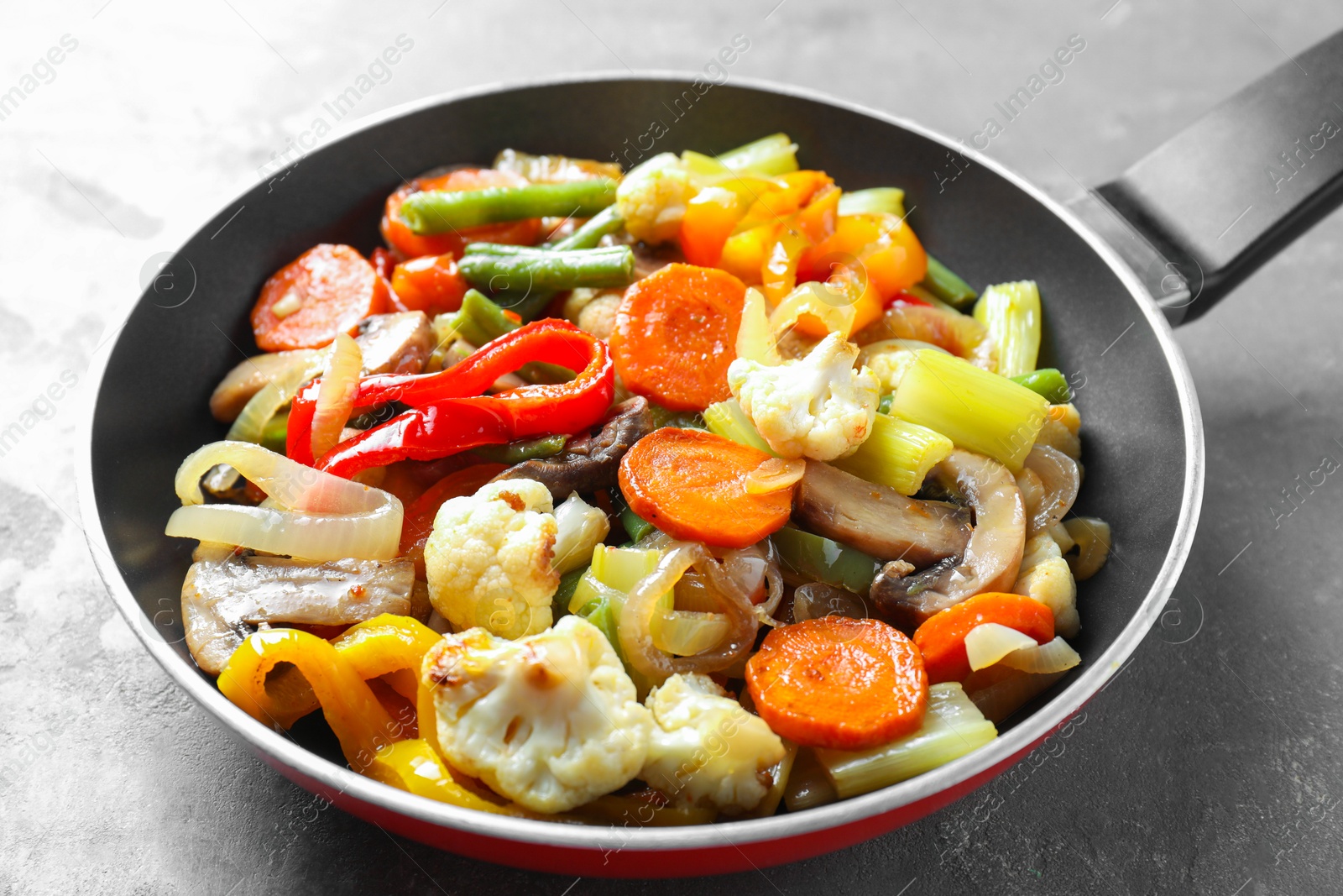 Photo of Different vegetables and mushrooms in frying pan on grey table, closeup