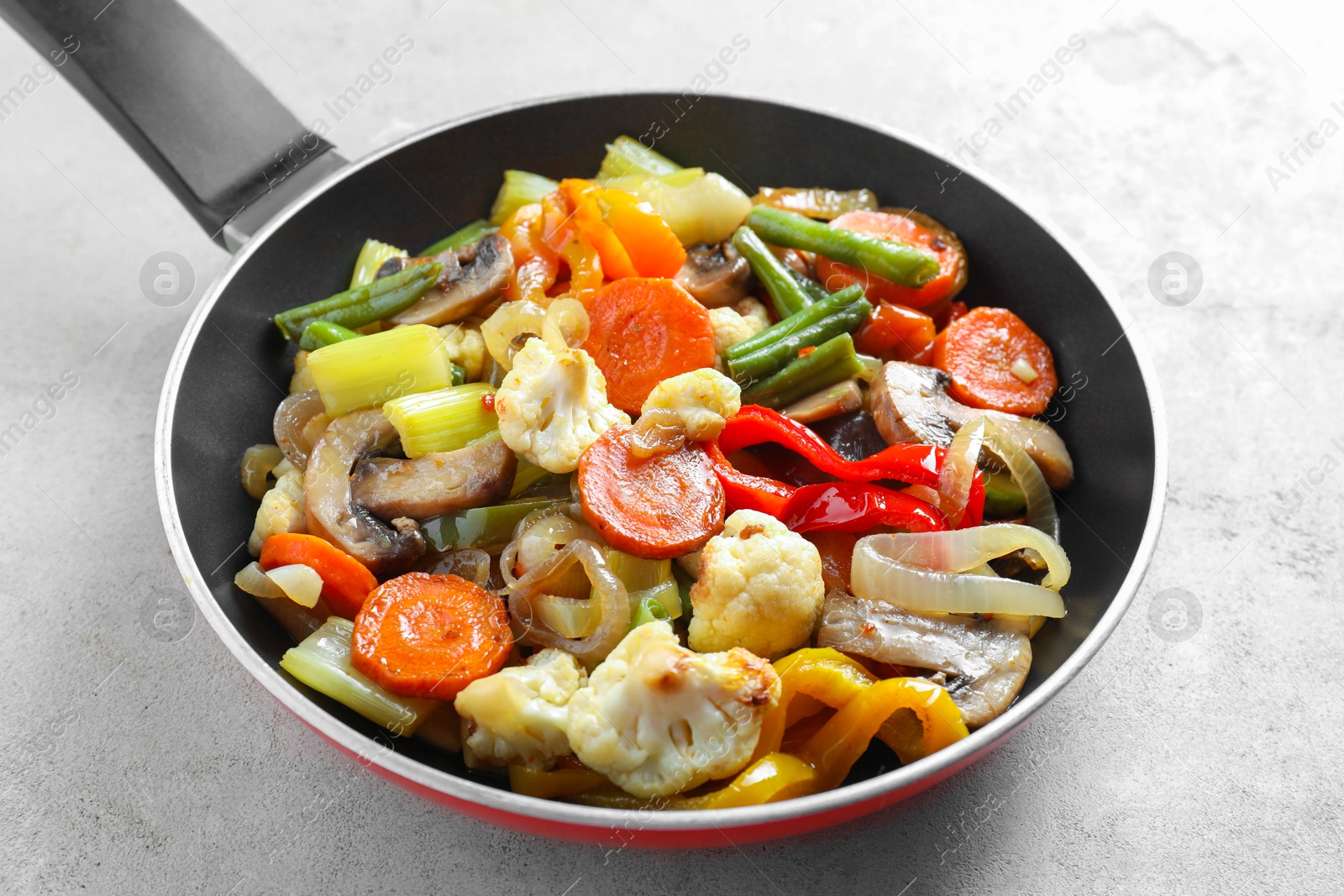 Photo of Different vegetables and mushrooms in frying pan on grey table, closeup