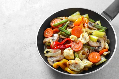 Photo of Different vegetables and mushrooms in frying pan on grey table, closeup. Space for text