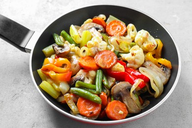 Photo of Different vegetables and mushrooms in frying pan on grey table, closeup