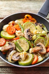 Photo of Different vegetables and mushrooms in frying pan on wooden table, closeup